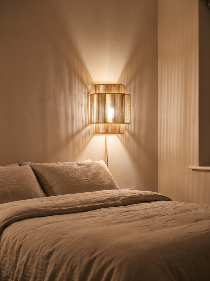 RattanGlow Handwoven Wall Lamp casting woven light patterns beside a bed