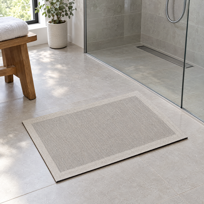 Oasis Quick-Dry Bath Mat in Taupe with Cream Border in front of a glass shower